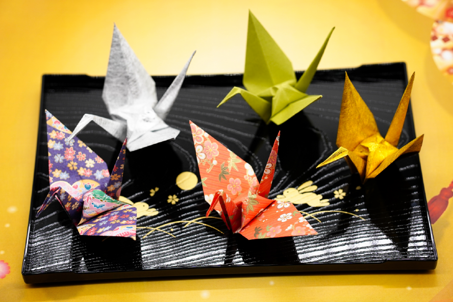 Sushi Origami Crane Combo with Chopstick Etiquette – Shodocafe 7557 Assorted sushi on a tray alongside decorative origami cranes and a pair of chopsticks demonstrating proper holding technique