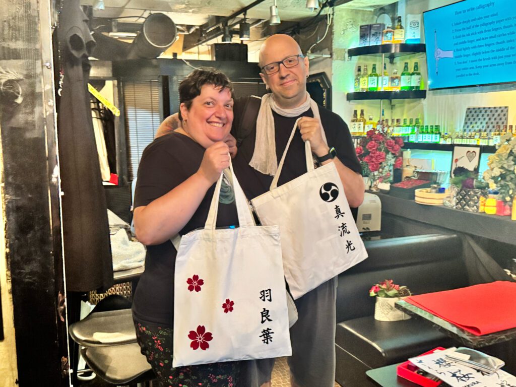 couple smiling custom kanji tote bags Top-selling custom kanji tote bag with sakura blossoms and a classic Mitsu-domoe crest, displayed at Shodocafe 7557 in Roppongi.
