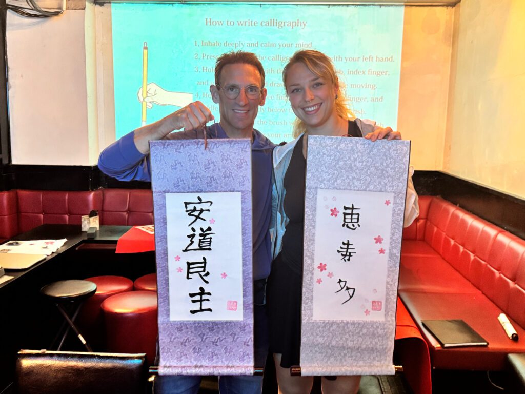 happy calligraphy guests scrolls shodocafe7557 1 Smiling couple holding custom kanji hanging scrolls – Shodocafe 7557 calligraphy class