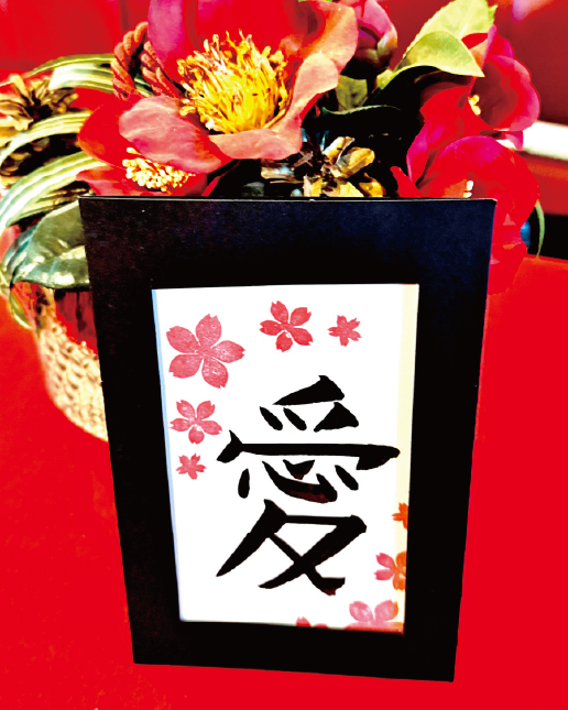 Calligraphy postcard featuring the kanji ‘ai’ (愛), decorated with cherry-blossom stamps in a black frame at Shodocafe7557 in Roppongi, Tokyo.