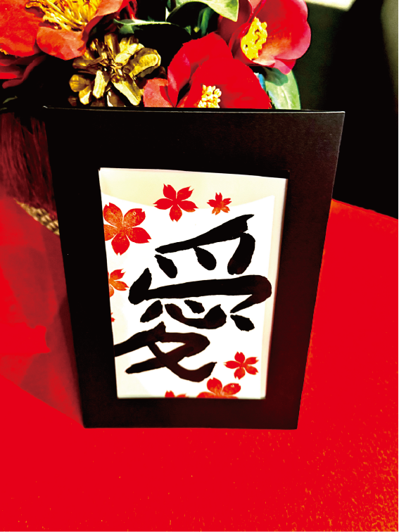 Calligraphy postcard featuring the kanji ‘ai’ (愛), decorated with cherry-blossom stamps in a black frame at Shodocafe7557 in Roppongi, Tokyo.