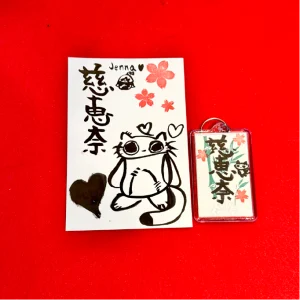 shodocafe7557 calligraphy postcard keychain jenna A personalized calligraphy postcard and keychain with the name ‘Jenna’ (慈恵奈) written in kanji at Shodocafe7557 in Roppongi, Tokyo. Includes sakura stamps and a cute cat illustration.