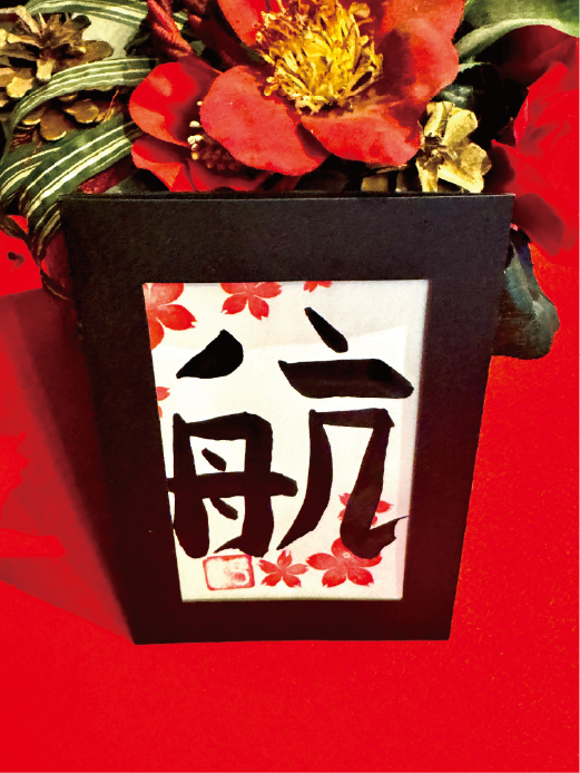 Calligraphy postcard featuring the kanji ‘kou’ (航), decorated with cherry-blossom stamps in a black frame at Shodocafe7557 in Roppongi, Tokyo.