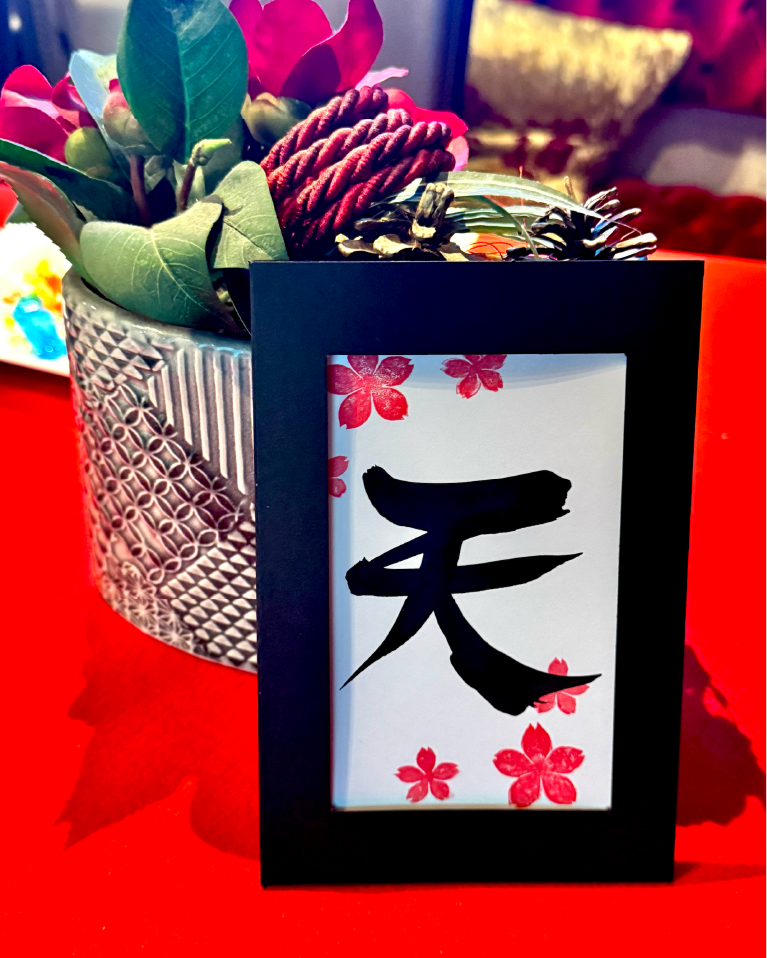 Calligraphy postcard featuring the kanji ‘ten’ (天), decorated with cherry-blossom stamps and bamboo accents in a black frame at Shodocafe7557 in Roppongi, Tokyo.