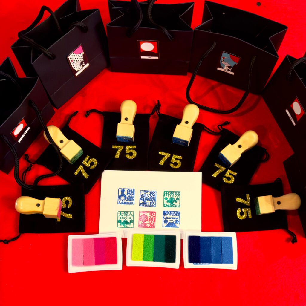 Set of personalized wooden kanji name hanko stamps with black pouches displayed on a red cloth at Shodocafe7557 in Roppongi, Tokyo—priced at ¥3,300 each with a complimentary video tutorial when booked in advance.