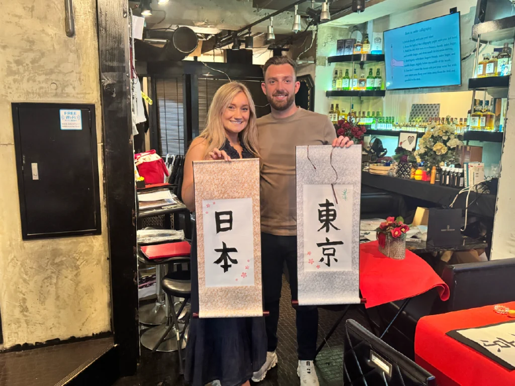 shodocafe7557 scroll Couple holding handmade kanji scrolls that read ‘Japan’ and ‘Tokyo’ at Shodocafe 7557 calligraphy class in Roppongi.