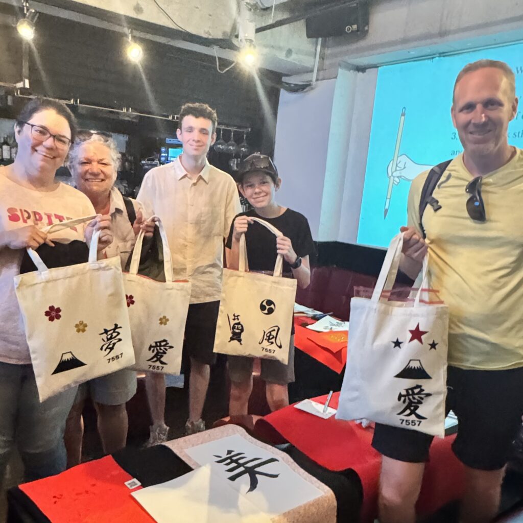 IMG 3935 Hotel guests at Shodocafe7557 in Tokyo display custom kanji tote bags featuring characters like ‘夢’ (dream), ‘愛’ (love), and ‘風’ (wind) created in the 50-minute calligraphy workshop.