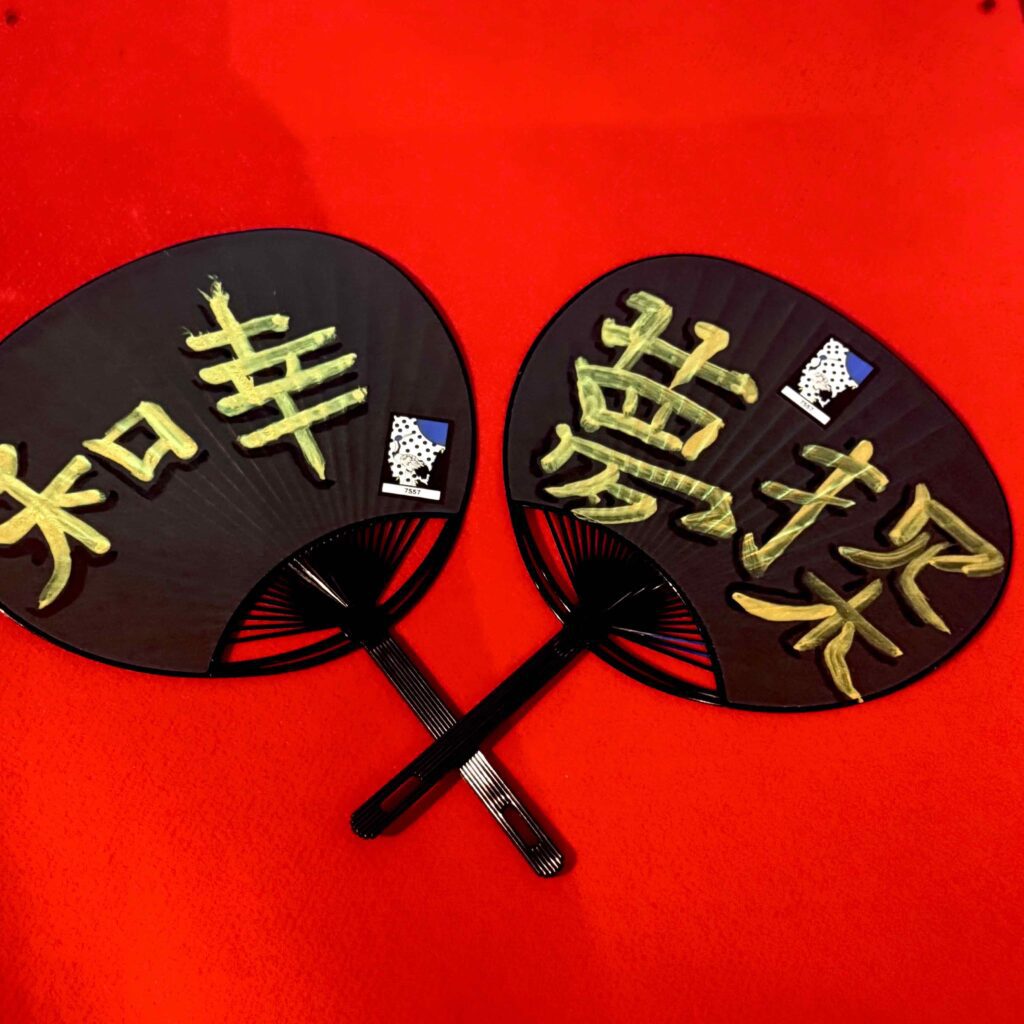 Japanese calligraphy on black uchiwa fans created during a workshop at Shodocafe7557 in Roppongi Tokyo — featuring golden kanji characters Japanese calligraphy on black uchiwa fans created at Shodocafe7557 in Roppongi, Tokyo — featuring golden kanji characters symbolizing wisdom, happiness, dreams, and exploration.