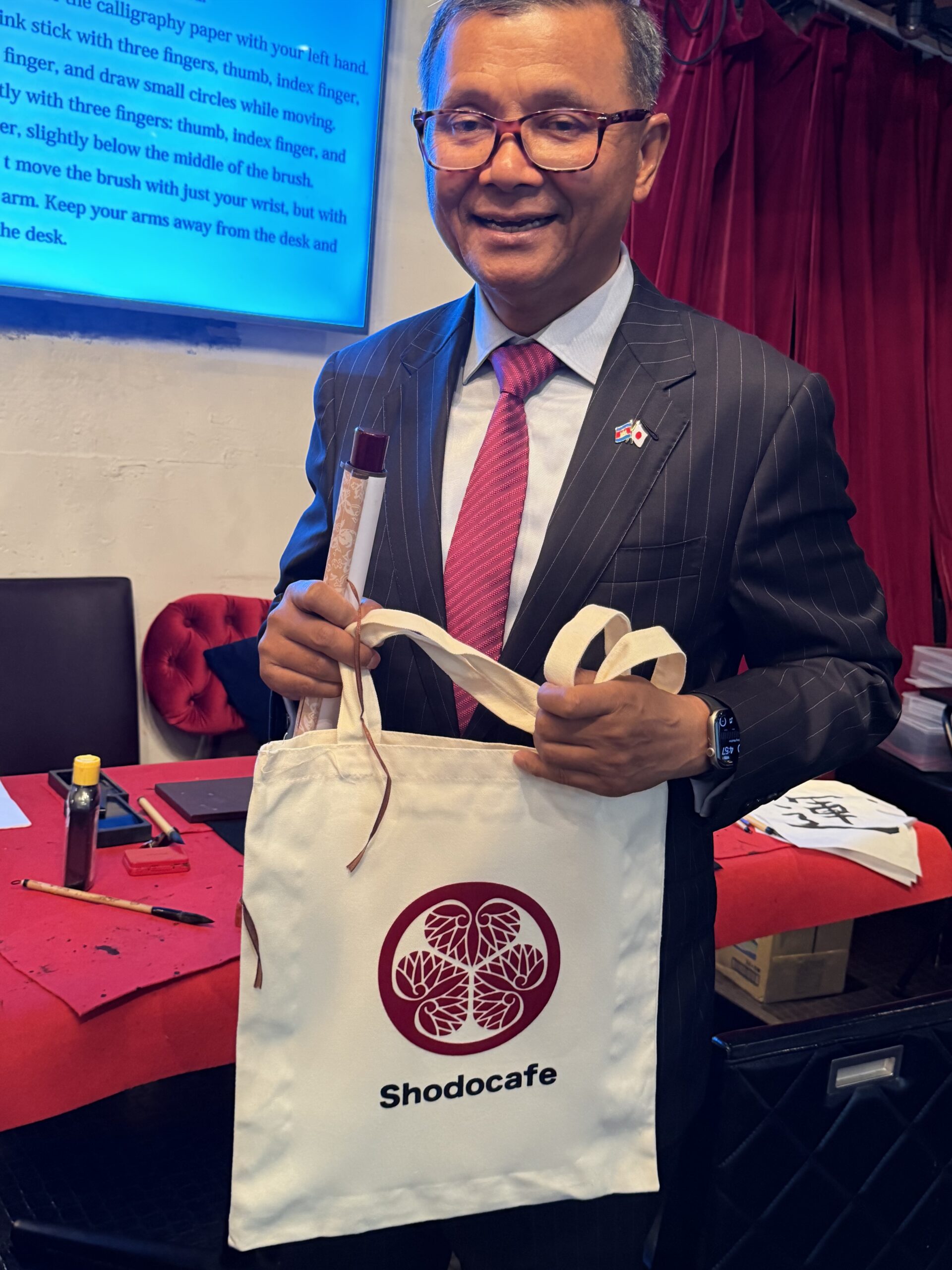 Cambodian Deputy Prime Minister Dr. Hang Chuon Naron holding a Japanese family crest tote bag received during a Japanese calligraphy experience at Shodocafe7557 in Roppongi, Tokyo.