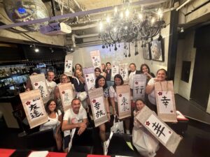 group calligraphy experience 16 guests shodocafe7557 tokyo 16 guests enjoying a private group Japanese calligraphy experience at Shodocafe7557 in Roppongi, Tokyo, holding their handmade Kanji hanging scrolls.